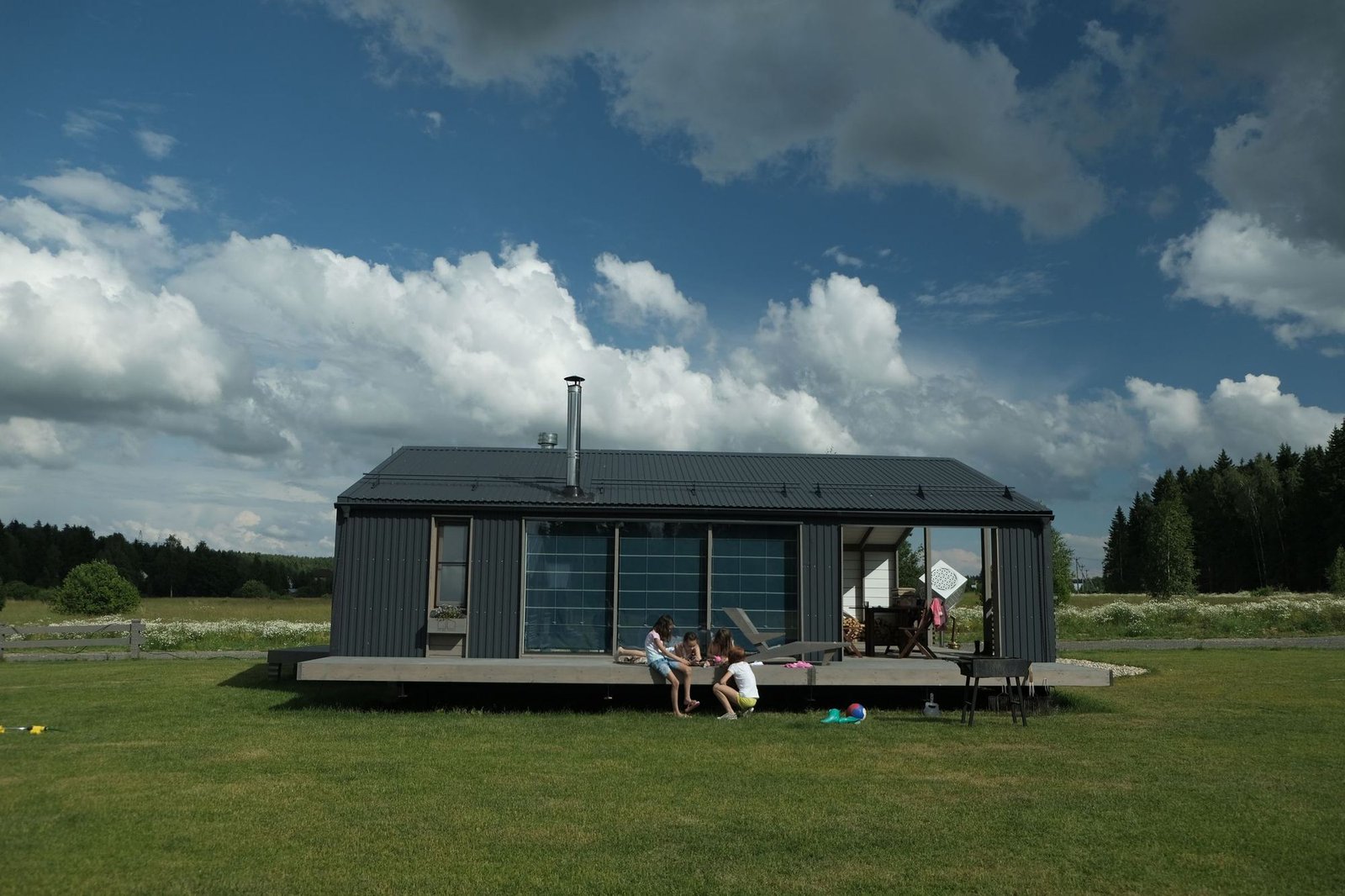 Casa modular térrea com deck e grandes janelas num prado, sob um céu com nuvens