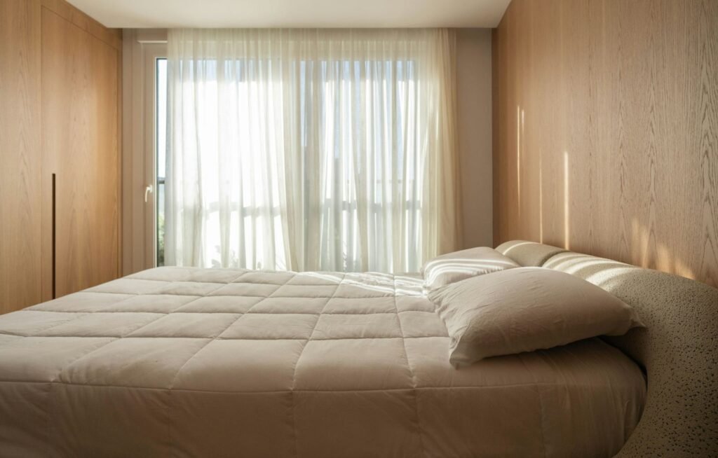 Quarto sereno com paredes revestidas a madeira e cortinas leves