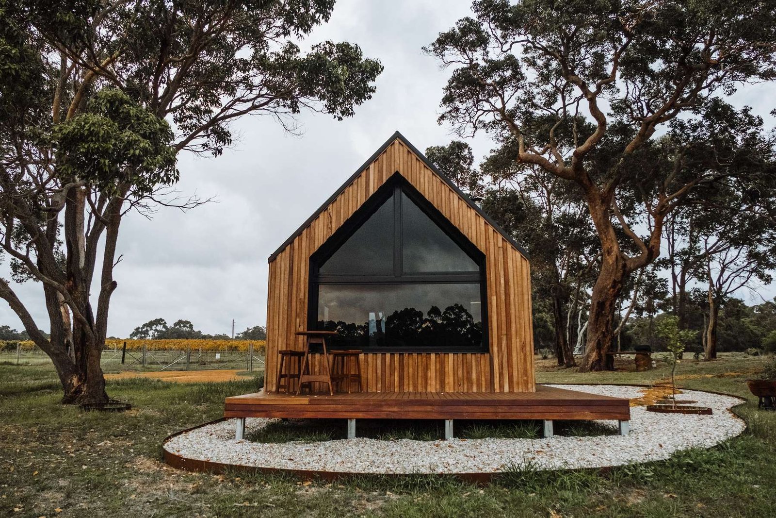 Pequena casa modular em madeira com grande envidraçado triangular e deck, entre eucaliptos