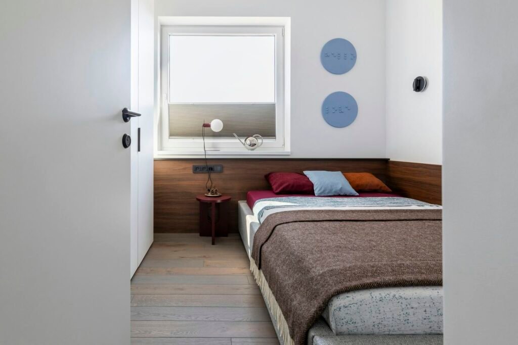 Quarto compacto com cabeceira em madeira e janela, em tons neutros
