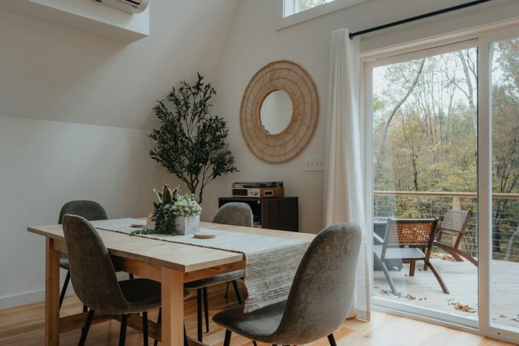 Zona de refeições compacta e luminosa com mesa de madeira e porta envidraçada para o terraço