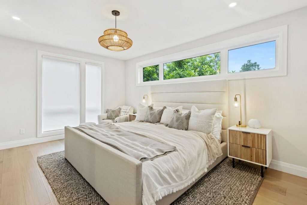 Quarto claro com janela alongada, candeeiro em fibra natural e roupa de cama em tons de areia