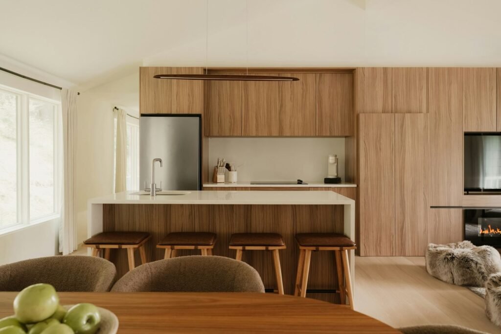Cozinha em madeira natural com ilha e bancos, integrada na sala