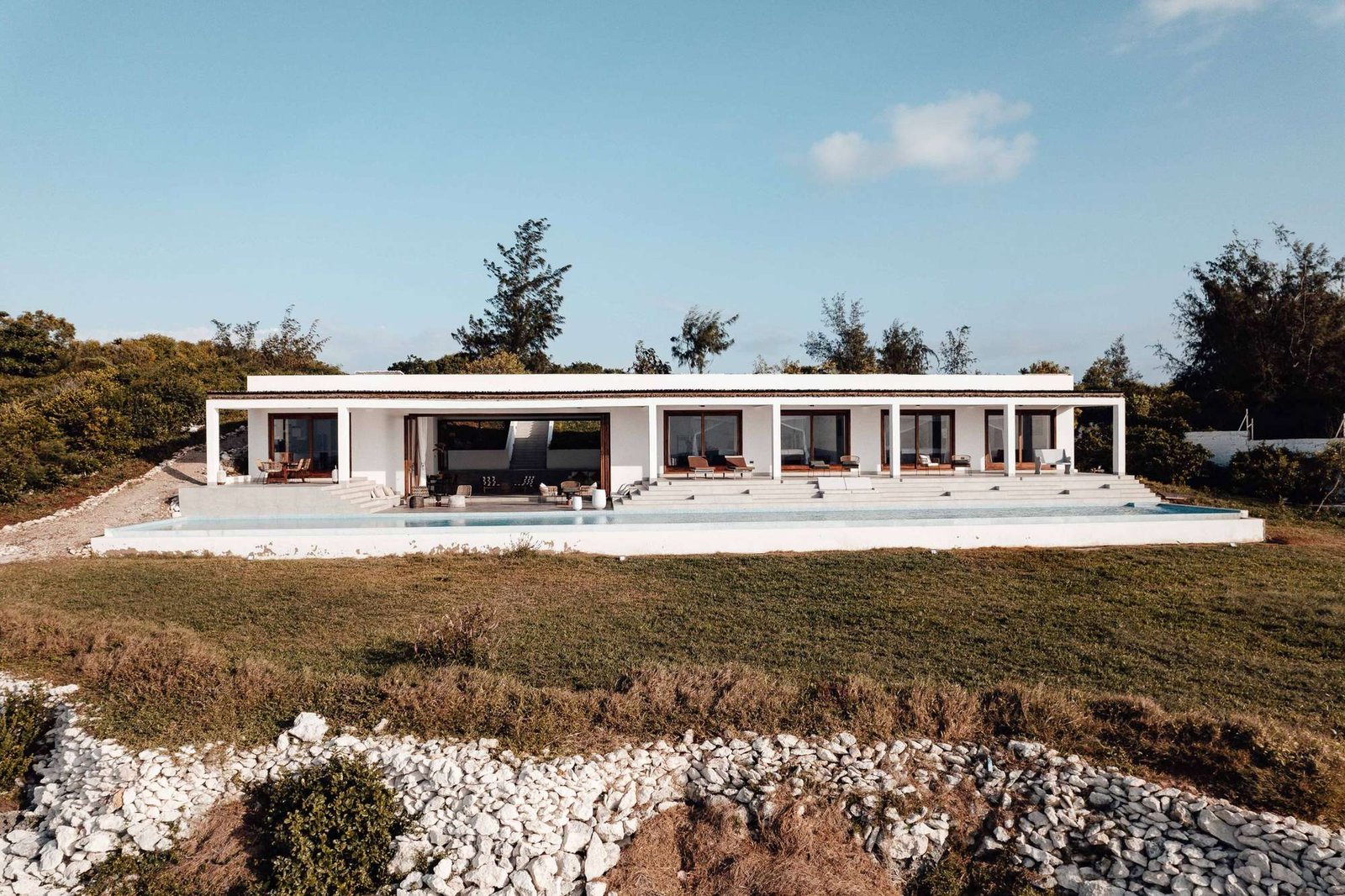 Casa térrea contemporânea de linhas brancas, com terraço e piscina, numa encosta com vegetação mediterrânica e céu limpo