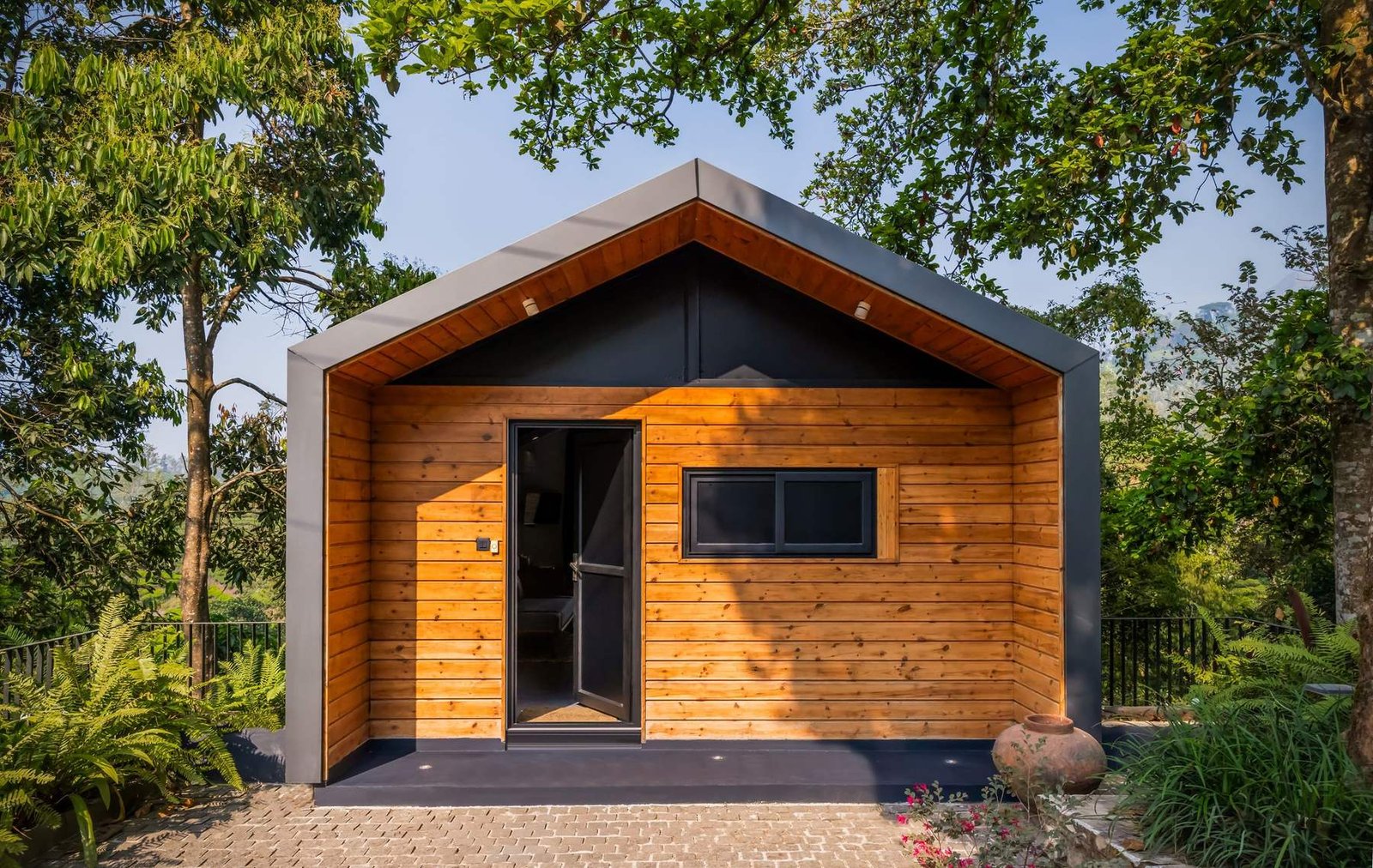 Casa modular de um só módulo com revestimento em madeira e moldura escura, rodeada de jardim