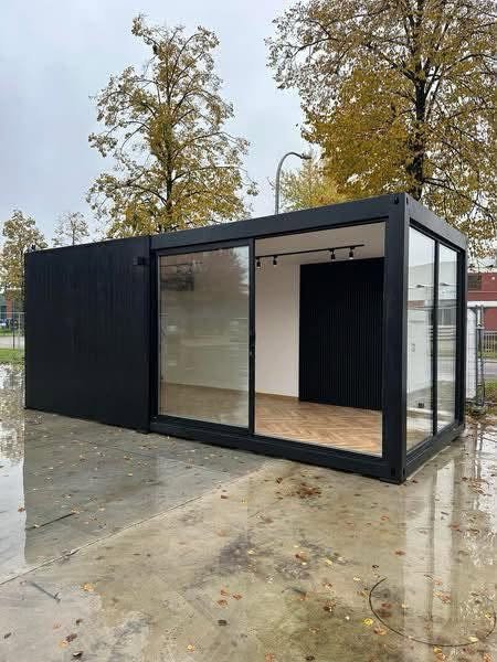Esquina envidraçada do edifício modular preto, com vista para o interior em pavimento de madeira