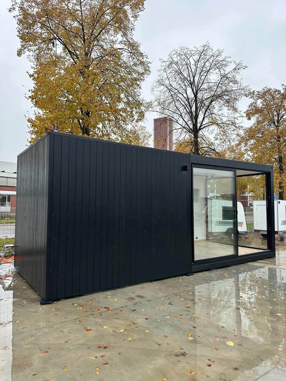 Edifício modular de 7 × 3 m com revestimento exterior em ripado vertical preto e porta de correr envidraçada