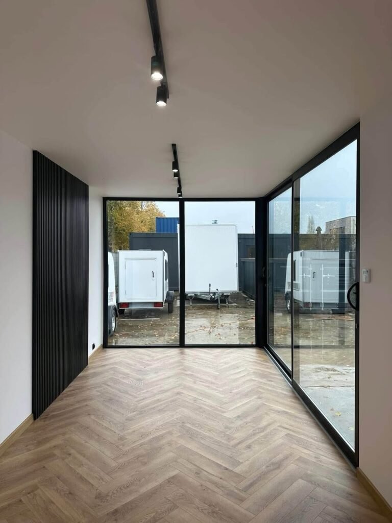 Espaço interior luminoso com pavimento em espinha, parede em ripado preto e vãos envidraçados em esquina